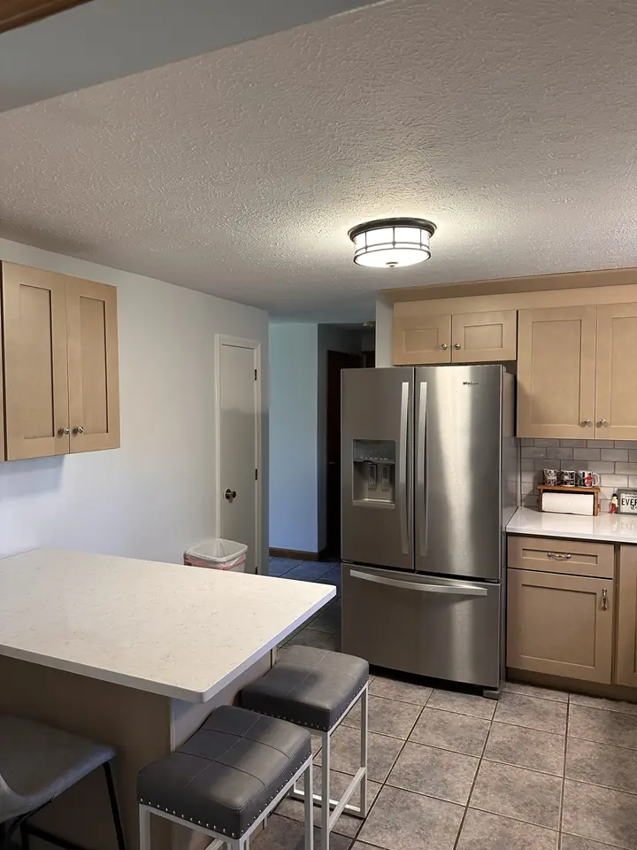 Remodeled kitchen with an island, bar stools, and stainless refrigerator by Dom's Workshop