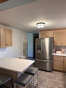 Remodeled kitchen with an island, bar stools, and stainless refrigerator by Dom's Workshop