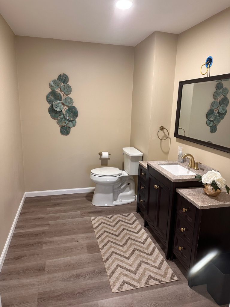 Remodeled bathroom with dark vanity, framed mirror, and plank flooring by Dom's Workshop
