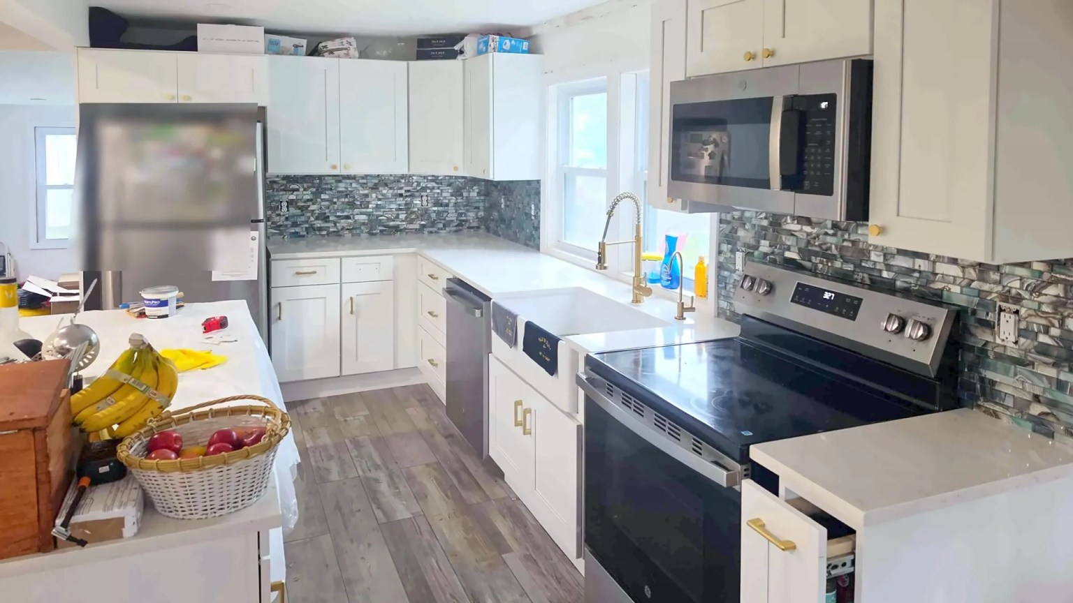 Renovated kitchen with white shaker cabinets, a farmhouse sink, a mosaic tile backsplash and stainless appliances.