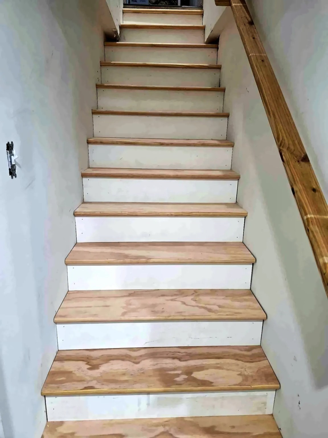 Rebuilt staircase with white risers, warm wood treads and a wall-mounted handrail in a whole-home renovation by Dom's Workshop